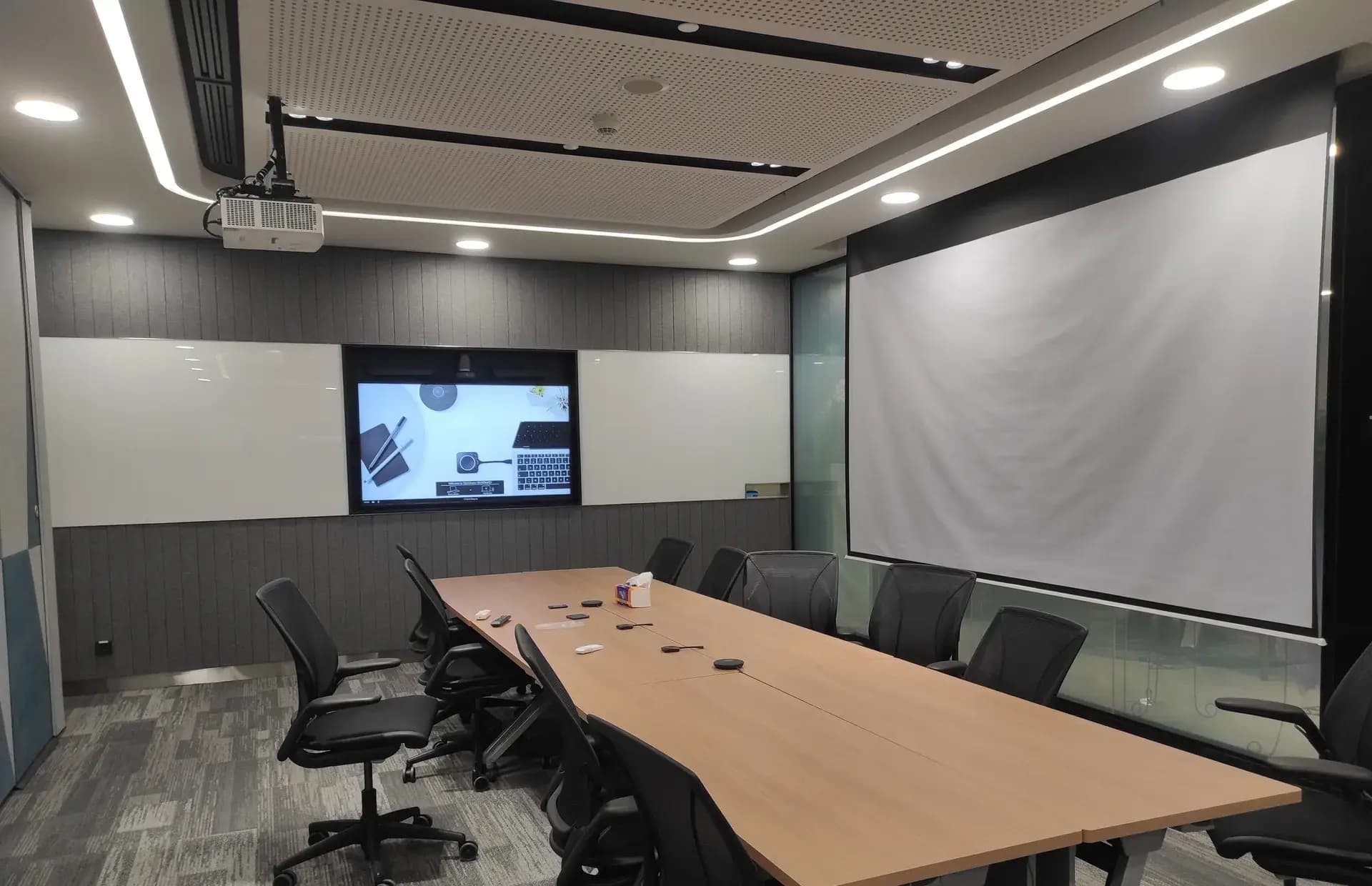 Ruang rapat dan training dengan proyektor, layar, display, serta plafon akustik — proyek sistem AV GVM